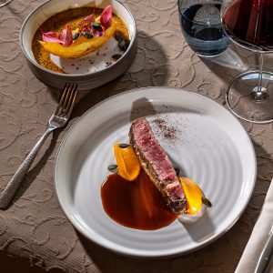 Das Bild zeigt ein köstliches Fleischgericht mit Beilagen und einem Rotweinglas daneben.