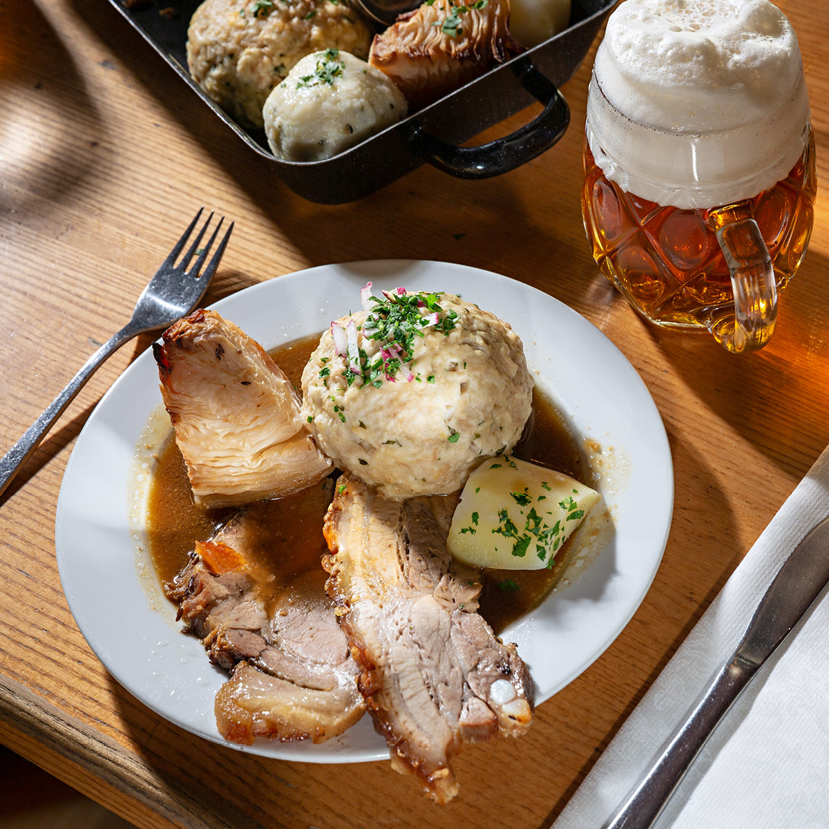 Das Bild zeigt ein köstliches Fleischgericht mit Beilagen und einem Bierglas daneben.